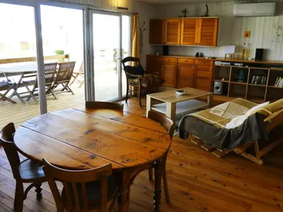 a living room with a wooden table and a kitchen at UN CHALET EN BOIS A LA PLAGE in Gruissan