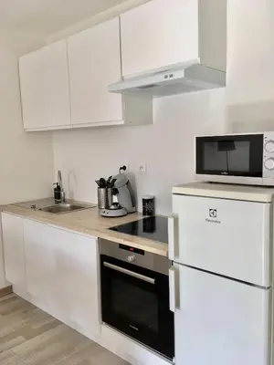a kitchen with white cabinets and a black appliance at Le cocon de Lenny in Conques-sur-Orbiel