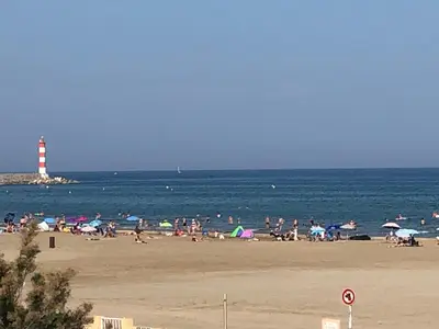 a group of people on a beach with a lighthouse at Appartement Vue Mer climatisé 2 chambres in Port-la-Nouvelle