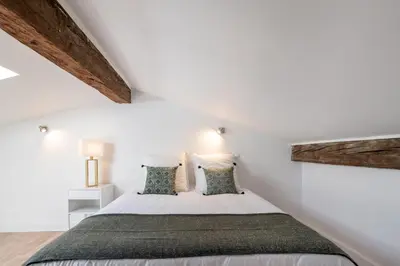 a bedroom with a bed with white walls and wooden beams at La suite numéro 1 in Carcassonne