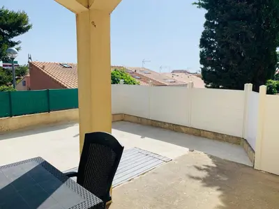 a table and a chair on a porch with a fence at La Pinède in Gruissan