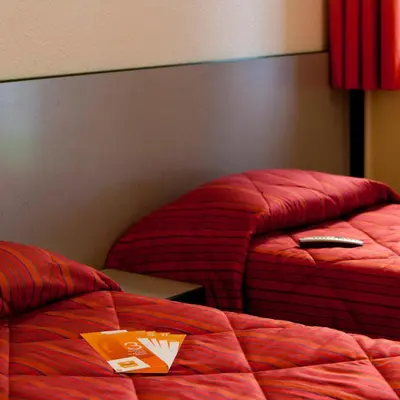 two beds with red comforters and a remote control on them at Hôtel Premiere Classe Pamiers in Pamiers