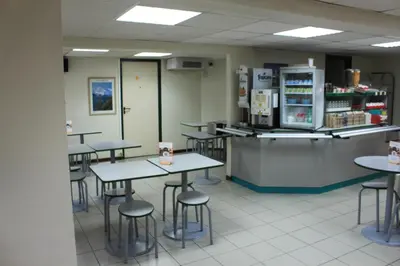 a cafeteria with tables and chairs and a refrigerator at Hôtel Premiere Classe Pamiers in Pamiers