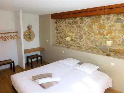a bedroom with a white bed and a stone wall at L'Accent d'ici in Le Somail