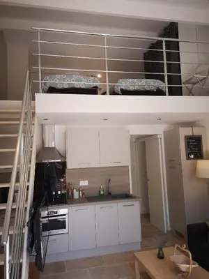 a small kitchen with white cabinets and a loft at Gîte Madeleine in Saint-Nazaire-dʼAude