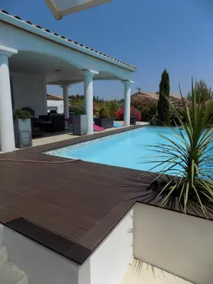 a swimming pool with a wooden deck next to a house at Villa VAYA in Villemoustaussou