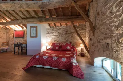 a bedroom with a red bed in a stone wall at Domaine de Malouziès in Fontiers-Cabardès