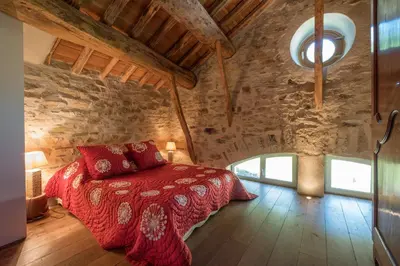 a bedroom with a red bed in a stone building at Domaine de Malouziès in Fontiers-Cabardès