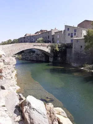 a bridge over a river next to some buildings at Chambre privée au coeur d'une pinède dans un quartier résidentiel in Lézignan-Corbières