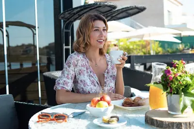 a woman sitting at a table with a cup of coffee at Hotel Le Phoebus Garden & Spa in Gruissan