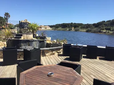 a wooden deck with a table and chairs next to a river at Hotel Le Phoebus Garden & Spa in Gruissan