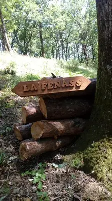 a sign sitting on logs next to a tree at la fenass in Noailhac