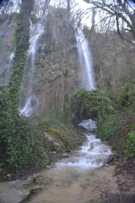 a waterfall on the side of a hill with a creek at Les Divines Cascades in Roquefort-les-Cascades