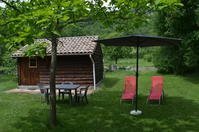 a table and chairs with an umbrella in front of a cabin at Les Divines Cascades in Roquefort-les-Cascades