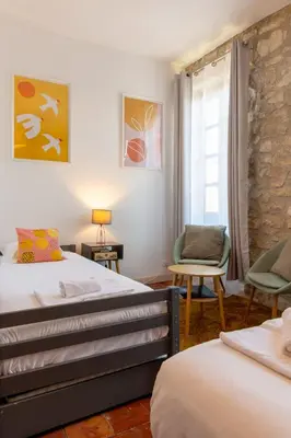 a bedroom with two beds and a chair and a window at Abitarela - Maison d'Hôtes - B&B in Sigean
