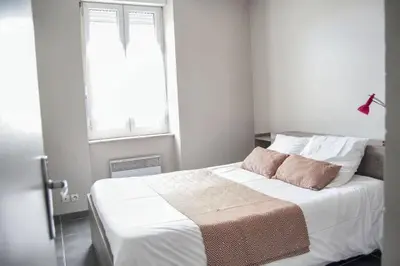 a bedroom with a bed with white sheets and a window at Appartement spacieux à Carcassonne 48 m² avec parking in Carcassonne