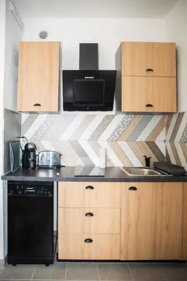 a kitchen with wooden cabinets and a black dishwasher at le studio du Grazel in Gruissan