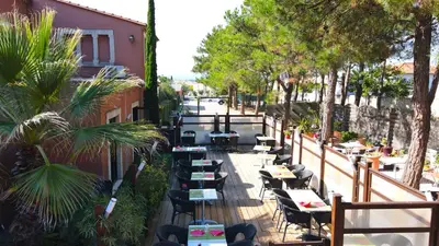 an outdoor patio with tables and chairs and trees at Hotel du Mas in Vinassan