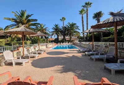 a resort pool with chairs and umbrellas and palm trees at Gite la Capelle près de Sigean Narbonne dans l'Aude à 10 min des plages Méditerranée in Roquefort-des-Corbières