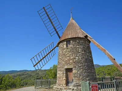 a stone windmill on a hill with mountains in the background at Modern villa in Camplong with private pool in Félines-Minervois
