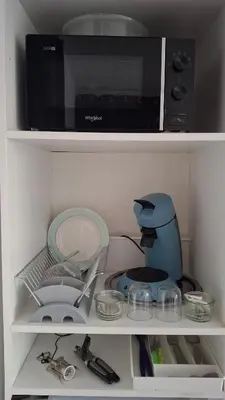 a kitchen shelf with a microwave and some dishes at Le Studio des 3 Moulins in Sigean