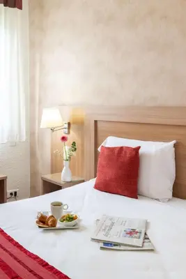 a bed with a red pillow and a plate of food on it at Brit Hotel Confort Castres in Castres