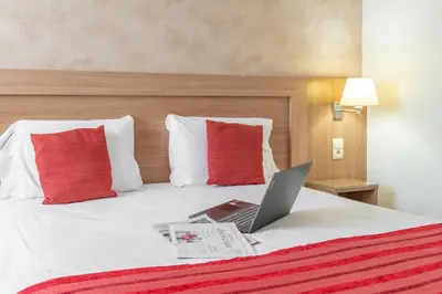 a laptop computer sitting on a bed with red pillows at Brit Hotel Confort Castres in Castres