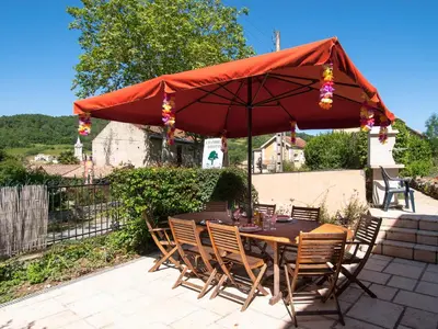 a wooden table and chairs under a red umbrella at Au Petit Verger in Puivert