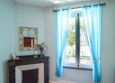 a room with a fireplace and a window with blue curtains at Au Petit Verger in Puivert