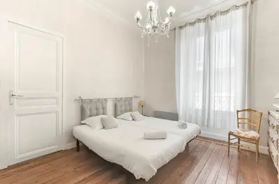 a white bedroom with a large bed and a chandelier at Les Bellevue Cité 