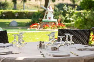 a table with wine glasses and a windmill in the background at Logis Hôtel et Restaurant La Bombardière in Cuq-Toulza