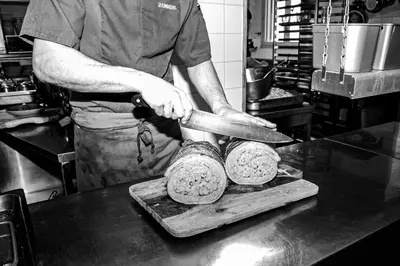 a man cutting food on a cutting board in a kitchen at Logis Hôtel et Restaurant La Bombardière in Cuq-Toulza