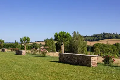 a yard with a stone wall in the grass at Logis Hôtel et Restaurant La Bombardière in Cuq-Toulza