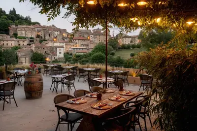 a patio with tables and chairs and a view of a city at Ecole Olargues - Chambres & restaurant - Teritoria in Olargues