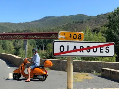 a man sitting on an orange scooter next to a sign at Ecole Olargues - Chambres & restaurant - Teritoria in Olargues
