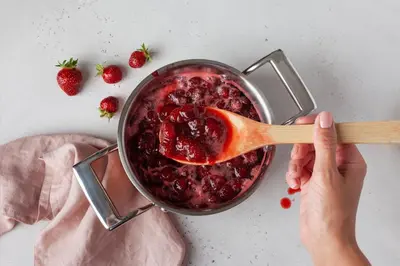 a person stirring a pot of strawberry jam with a wooden spoon at La Lagune in Bages