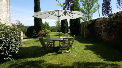a table and chairs under an umbrella in the grass at Domaine de Las Planques in Vaudreuille