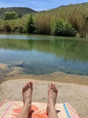 a persons feet on a blanket next to a body of water at Le Sommet in Paziols