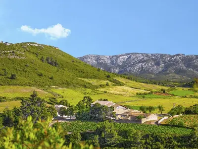a green hill with a village and mountains in the background at Cozy Escape in Villesèque in Villesèque-des-Corbières