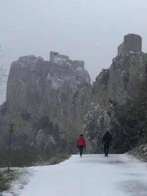 two people walking down a snow covered road with a castle at Gîte San Jordi in Duilhac
