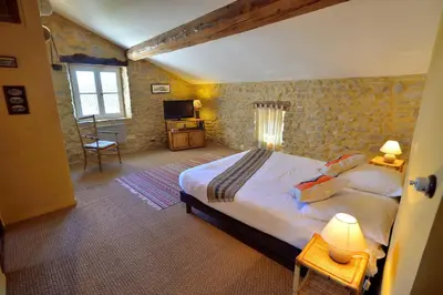 a bedroom with a large bed and a stone wall at Le village-hôtes in Sainte-Vallière