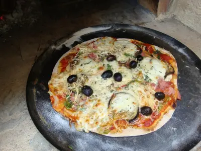 a pizza with black olives and cheese on a pan at Le village-hôtes in Sainte-Vallière