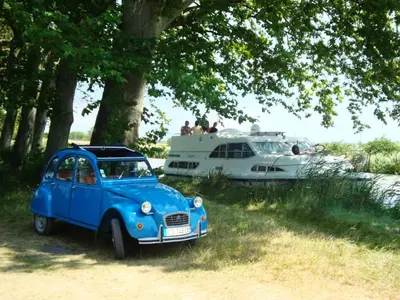 an old blue car parked next to a boat at Le village-hôtes in Sainte-Vallière