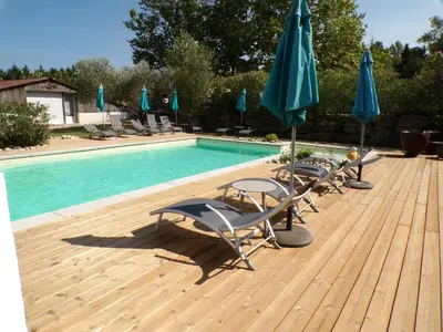a deck with chairs and umbrellas next to a swimming pool at Gîte le Relais de la Cavayere in Carcassonne