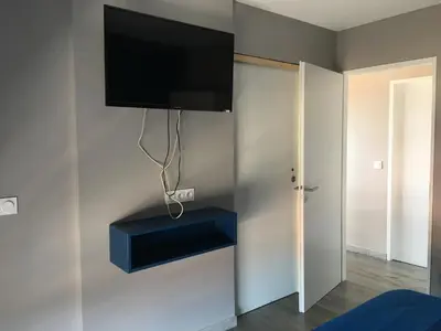 a flat screen tv hanging on a wall with a blue shelf at Fun and sun room in Salles-d'Aude