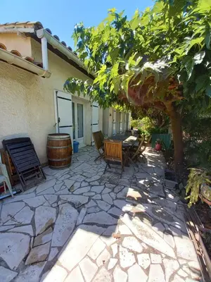 a patio with a tree and chairs and a barrel at Los olivos in Bize-Minervois
