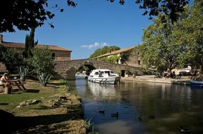 a boat in a river with a bridge and ducks at Gîte Esprit Loft Proche de Narbonne in Mirepeisset