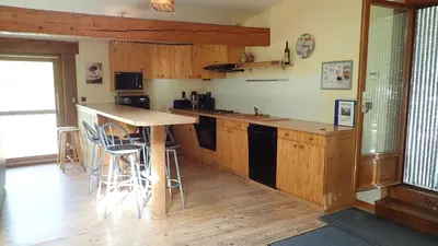 a kitchen with wooden cabinets and a bar with stools at Gîtes Le Paradoxe des Pyrénées in Montferrier