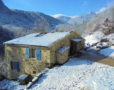 a stone house in the snow with mountains in the background at Gîtes Le Paradoxe des Pyrénées in Montferrier
