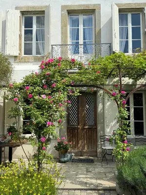 an arch with pink flowers in front of a house at Le Patio Des Senteurs in Verzeille